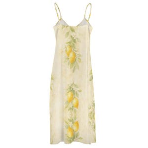 The back of a light yellow spaghetti strap maxi dress with a lemon and leaf print hangs on a wooden hanger.
