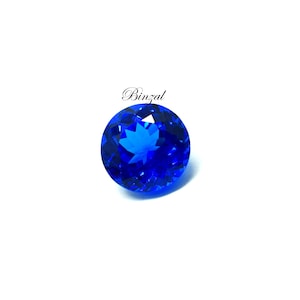 May include: A round, faceted, brilliant blue gemstone. The gem has a star-like pattern in the center and is set against a white background. The word "Binzal" is written in cursive above the gem.