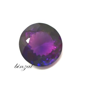May include: A faceted, round gemstone with a gradient of purple and blue hues. The gem has a polished surface and is set against a white background. The word "binzal" is written in cursive on the lower left.