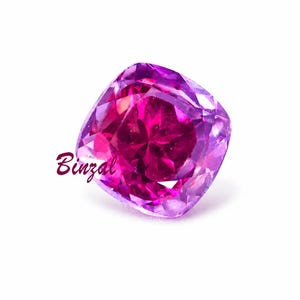 May include: A cushion-cut gemstone with a vibrant pink center and a lighter purple hue towards the edges. The gem is set against a white background. The word "Binzal" is written in a cursive font.