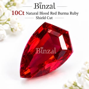 Op de afbeelding: Een 10 karaat natuurlijke bloedrode Birma robijn met een schildslijpvorm. De edelsteen heeft een gefacetteerd oppervlak en wordt getoond met de tekst Binzal 10Ct Natural Blood Red Burma Ruby Shield Cut erboven en de merknaam Binzal op de steen.