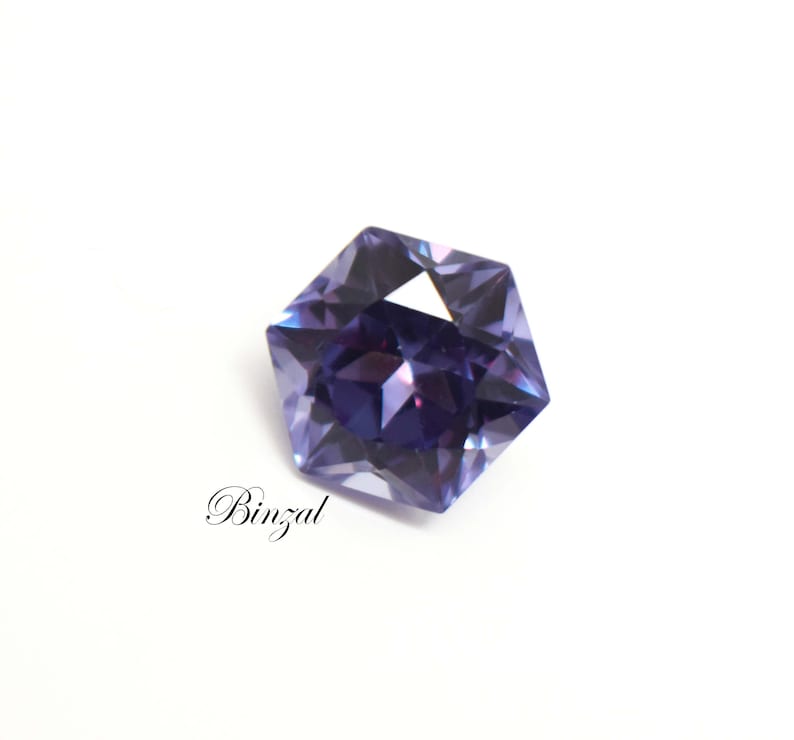 Puede incluir: Una piedra preciosa morada de forma pentagonal con facetas y un corte brillante que refleja la luz. La piedra muestra tonos violeta intenso y lavanda m&aacute;s claro en toda su superficie. La palabra Binzal est&aacute; impresa en texto negro.