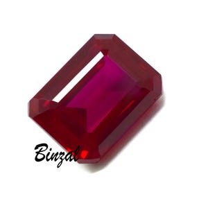 May include: A rectangular-cut ruby gemstone with a deep red colour. The gem has a polished surface and a vibrant, internal colour. The word "Binzal" is written in cursive on the lower left side of the gem.