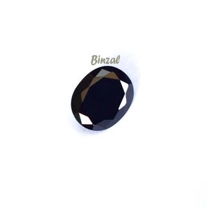 May include: A faceted, oval-shaped, dark blue gemstone. The gem has a polished surface with multiple facets that reflect light. The word "Binzal" is printed in light gray above the gemstone.
