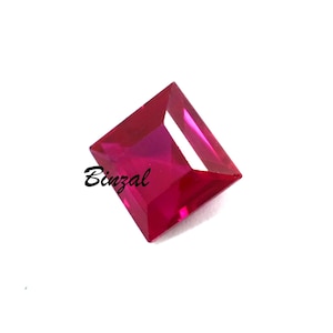 May include: A square-cut ruby gemstone in a rich red colour. The gem is faceted, reflecting light and displaying its clarity. The word "Binzal" is written on the gem.