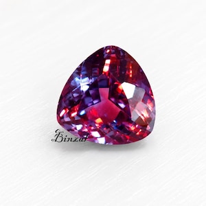 May include: A faceted, heart-shaped gemstone with a color-shifting effect. The gem transitions from deep purple to a vibrant red hue, with internal light reflections. The word "Binzal" is written on the bottom left of the gem.