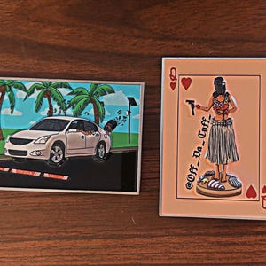 May include: Two metal pins. One features a white car driving past palm trees, with a black object flying out the window. The other pin is a playing card with a woman in a hula skirt holding a gun, with the text "Off_Do_Cuff".