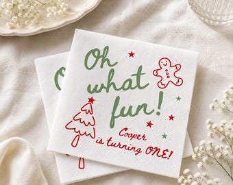 May include: White paper napkins featuring green text that reads Oh what fun! and red text that reads Cooper is turning ONE!. The design includes a red gingerbread man, a red Christmas tree, and small red and green stars.
