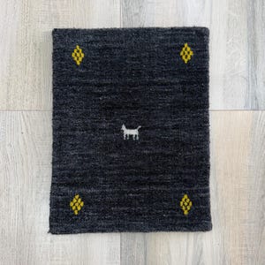 May include: A dark gray rectangular rug with a small white dog silhouette in the center. The rug has four yellow diamond-shaped patterns, one in each corner. The rug is made of a textured material.