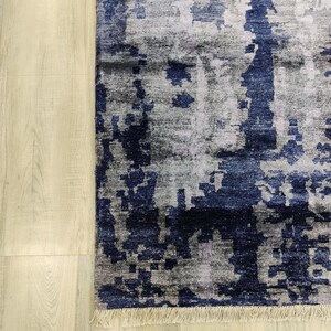 Puede incluir: Una alfombra rectangular con un patr&oacute;n abstracto en tonos azul marino profundo, gris carb&oacute;n y plata claro. El dise&ntilde;o consiste en formas fragmentadas y pixeladas con vetas verticales, rematado con un fleco corto de color claro.