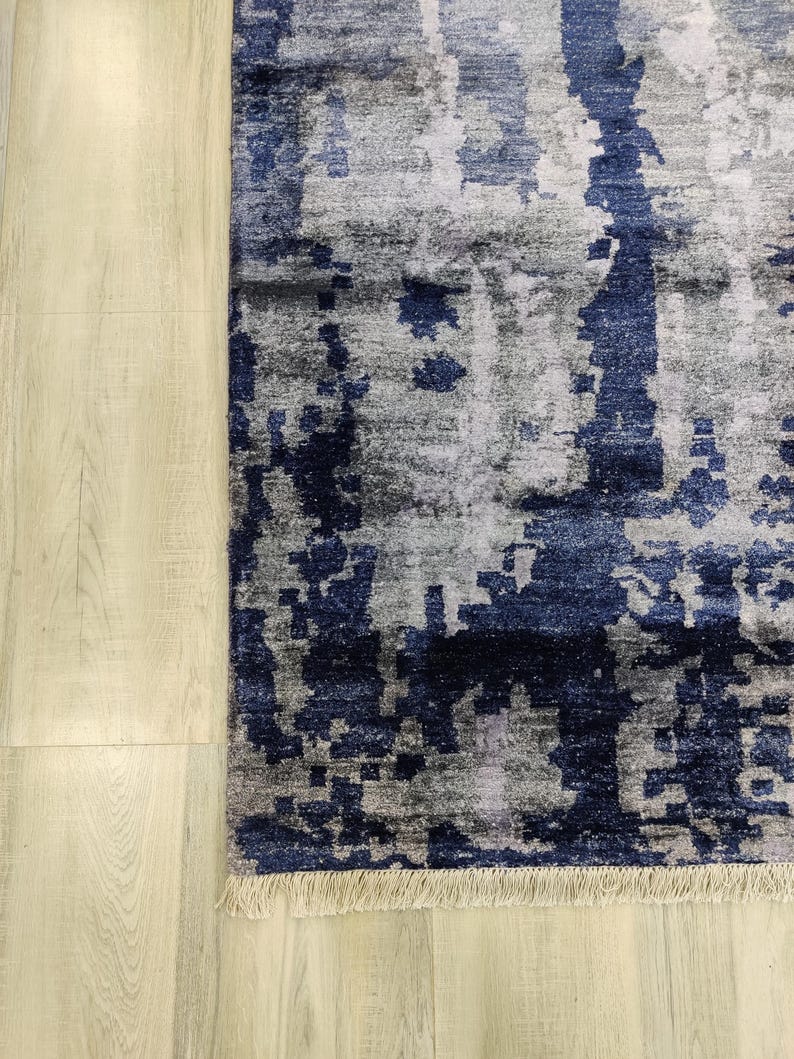Puede incluir: Una alfombra rectangular con un patr&oacute;n abstracto en tonos azul marino profundo, gris carb&oacute;n y plata claro. El dise&ntilde;o consiste en formas fragmentadas y pixeladas con vetas verticales, rematado con un fleco corto de color claro.