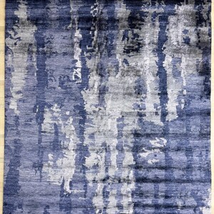 Puede incluir: Una alfombra rectangular con un patr&oacute;n abstracto de rayas verticales en tonos azul marino, gris pizarra y blanco. El dise&ntilde;o muestra una apariencia texturizada y superpuesta con un fleco corto en los bordes superior e inferior.