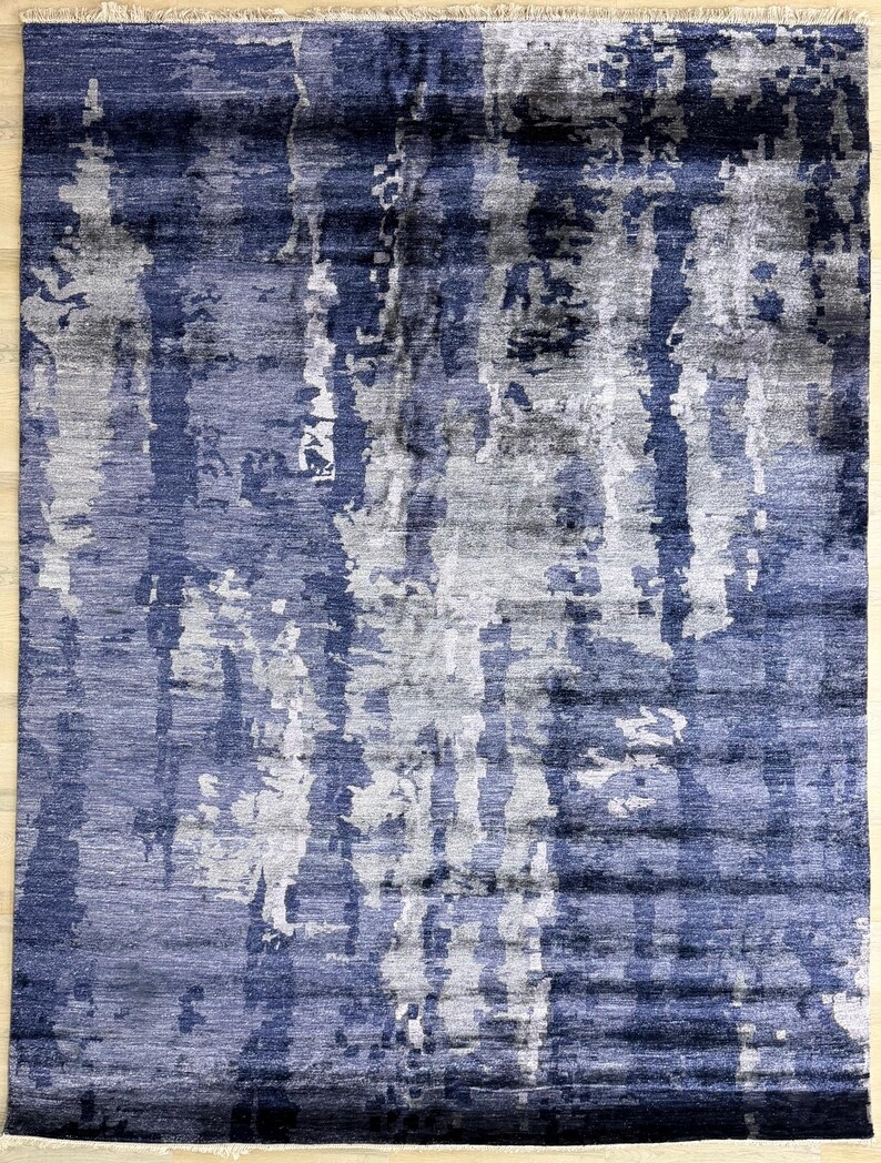 Puede incluir: Una alfombra rectangular con un patr&oacute;n abstracto de rayas verticales en tonos azul marino, gris pizarra y blanco. El dise&ntilde;o muestra una apariencia texturizada y superpuesta con un fleco corto en los bordes superior e inferior.