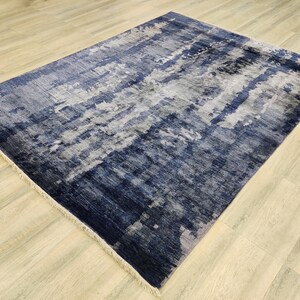 Puede incluir: Una alfombra rectangular con un patr&oacute;n abstracto en tonos azul marino, gris pizarra y blanco. El dise&ntilde;o consiste en bandas horizontales texturizadas superpuestas y parches moteados. La alfombra tiene flecos cortos de color claro en los extremos.