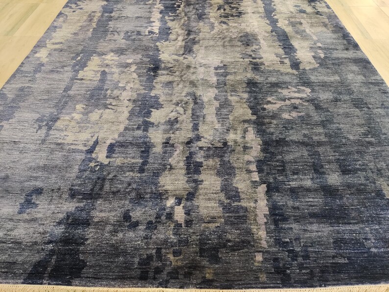 Puede incluir: Una alfombra rectangular con un patr&oacute;n abstracto de tonos mezclados en azul marino, gris pizarra y blanco roto. El dise&ntilde;o consiste en variaciones de color verticales y veteadas con una apariencia tejida y un fleco corto en el borde.
