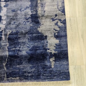 Puede incluir: Una alfombra rectangular con un patr&oacute;n abstracto en tonos azul marino profundo, azul real y gris claro. El dise&ntilde;o consiste en bloques de color verticales y texturizados con parches moteados. La alfombra est&aacute; terminada con un fleco corto de color beige.
