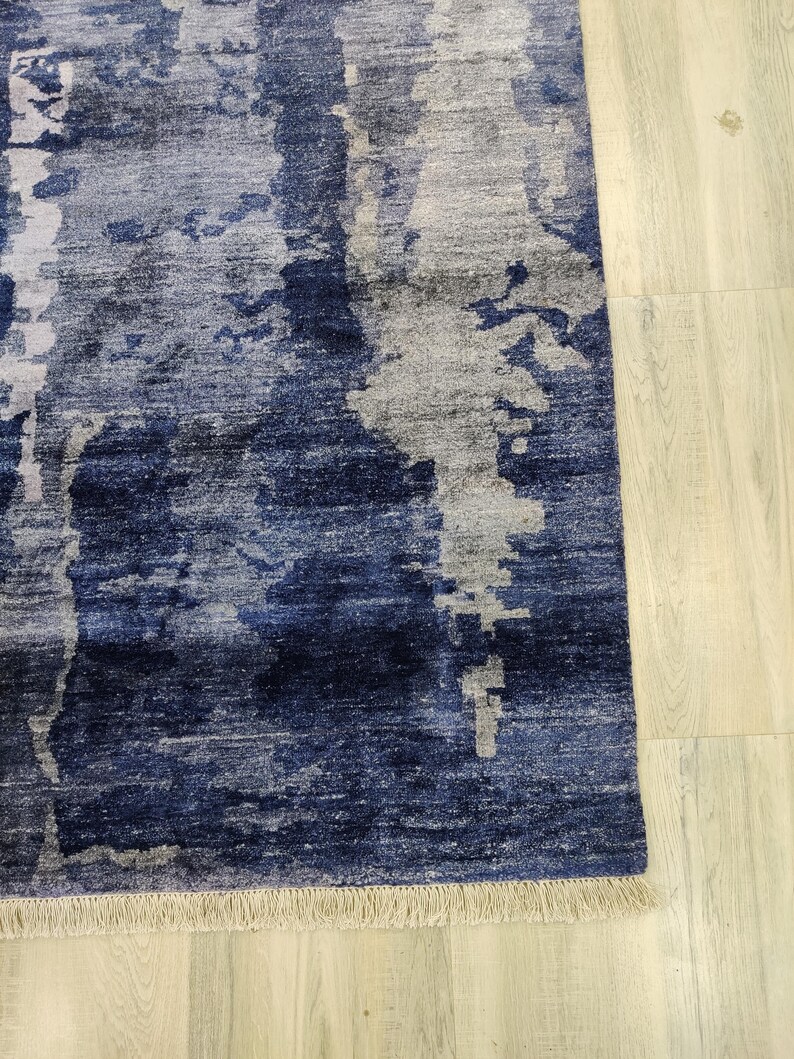 Puede incluir: Una alfombra rectangular con un patr&oacute;n abstracto en tonos azul marino profundo, azul real y gris claro. El dise&ntilde;o consiste en bloques de color verticales y texturizados con parches moteados. La alfombra est&aacute; terminada con un fleco corto de color beige.