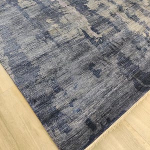 Puede incluir: Una alfombra rectangular con un patr&oacute;n abstracto en tonos azul marino, gris pizarra y blanco. El dise&ntilde;o muestra una apariencia texturizada y desgastada con variaciones de color verticales y un fleco corto de color crema en el borde.