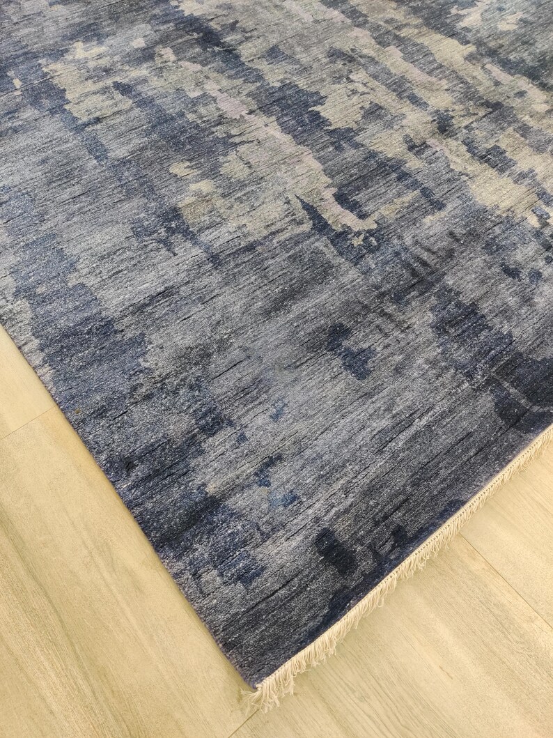 Puede incluir: Una alfombra rectangular con un patr&oacute;n abstracto en tonos azul marino, gris pizarra y blanco. El dise&ntilde;o muestra una apariencia texturizada y desgastada con variaciones de color verticales y un fleco corto de color crema en el borde.