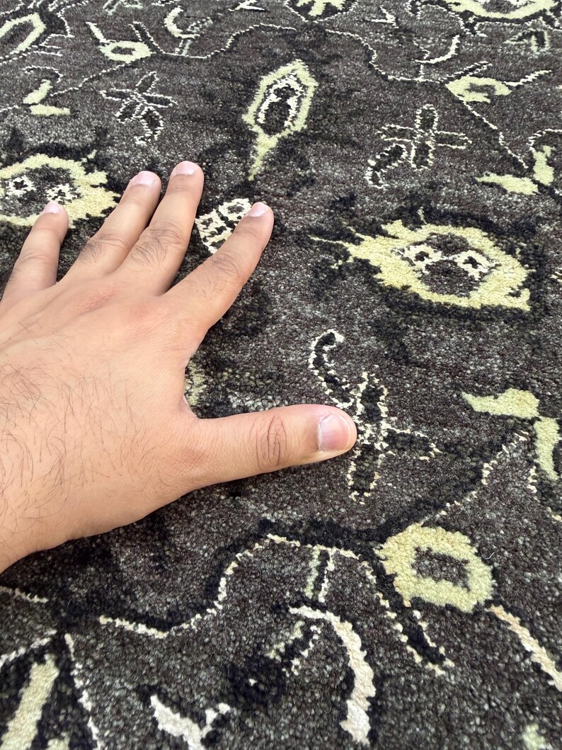 Puede incluir: Una alfombra de color gris carb&oacute;n oscuro con un patr&oacute;n repetitivo de motivos florales y geom&eacute;tricos en color crema claro. La superficie de la alfombra tiene un pelo denso y texturizado con fibras visibles en los dise&ntilde;os.