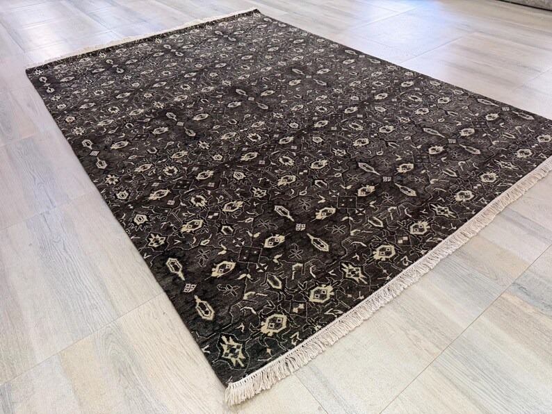 Puede incluir: Una alfombra rectangular con fondo marr&oacute;n oscuro y un intrincado patr&oacute;n geom&eacute;trico repetitivo en crema y beige claro. La alfombra tiene una textura de pelo corto y est&aacute; rematada con flecos de color crema en los dos extremos m&aacute;s cortos.