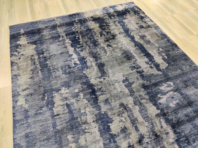 Puede incluir: Una alfombra rectangular con un patr&oacute;n abstracto y texturizado en tonos azul marino profundo, gris pizarra y plata claro. El dise&ntilde;o consiste en rayas verticales de aspecto desgastado y parches moteados que crean una apariencia en capas.