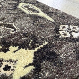 Puede incluir: Una alfombra gruesa y texturizada con una base de color gris carb&oacute;n oscuro y marr&oacute;n oscuro, con patrones abstractos florales y geom&eacute;tricos de color crema tejidos en el pelo denso y afelpado de la superficie.