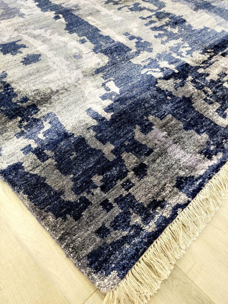 Puede incluir: Una alfombra rectangular con un patr&oacute;n abstracto en tonos azul marino, gris pizarra y blanco. La alfombra tiene una superficie de pelo texturizado y est&aacute; rematada con una hilera de flecos de color crema a lo largo del borde corto.