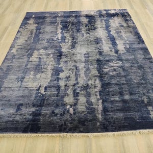 Puede incluir: Una alfombra rectangular con un patr&oacute;n abstracto en tonos azul marino profundo, gris pizarra y blanco. El dise&ntilde;o consiste en variaciones de color verticales y veteadas con una apariencia texturizada y flecos cortos en los bordes.