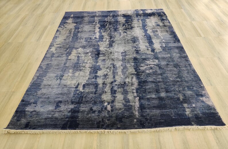 Puede incluir: Una alfombra rectangular con un patr&oacute;n abstracto en tonos azul marino profundo, gris pizarra y blanco. El dise&ntilde;o consiste en variaciones de color verticales y veteadas con una apariencia texturizada y flecos cortos en los bordes.