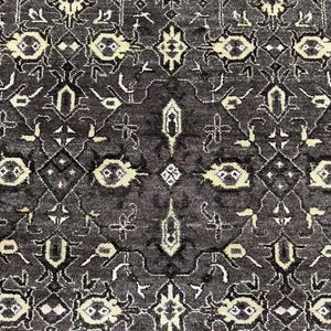 Puede incluir: Una alfombra de color gris carb&oacute;n oscuro con un patr&oacute;n sim&eacute;trico repetitivo de motivos florales y geom&eacute;tricos en tonos crema y beige claro. El dise&ntilde;o intrincado consta de formas interconectadas y elementos bot&aacute;nicos estilizados.