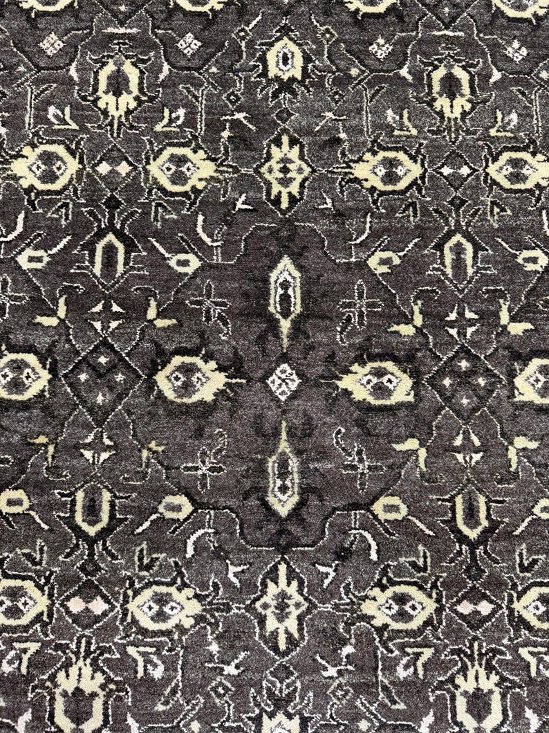 Puede incluir: Una alfombra de color gris carb&oacute;n oscuro con un patr&oacute;n sim&eacute;trico repetitivo de motivos florales y geom&eacute;tricos en tonos crema y beige claro. El dise&ntilde;o intrincado consta de formas interconectadas y elementos bot&aacute;nicos estilizados.