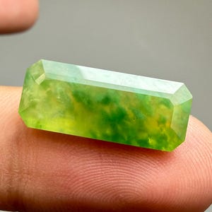 Peut inclure: Une pierre précieuse rectangulaire à facettes avec un aspect translucide, présentant un mélange vibrant de teintes vert citron et vert jaune avec des inclusions nuageuses internes et une surface polie et lisse reflétant la lumière.
