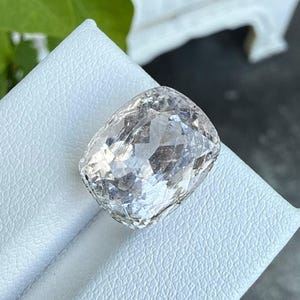 Könnte beinhalten: Ein farbloser Edelstein im Kissenschliff mit einer facettierten Oberfläche, die das Licht reflektiert. Der Stein hat eine rechteckige Form mit abgerundeten Ecken und ein klares, transparentes Aussehen mit vielen geometrischen Facetten.