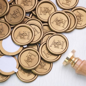 May include: Gold wax seals with the initials "AH" in a serif font. The seals are round and have a raised border. A brass seal stamp with a wooden handle is in the lower right corner. Some seals have adhesive backing.