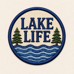 May include: A circular embroidered patch featuring the text LAKE LIFE in dark blue letters. The design includes two green pine trees on either side and stylized wavy blue water lines at the bottom, all enclosed within a dark blue stitched border.