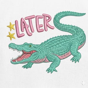 May include: An embroidered design featuring a teal alligator with an open mouth, revealing a pink interior. The word "LATER" is in pink above the alligator, with two yellow stars. The design is on a white background.