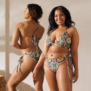 Könnte beinhalten: Zweiteiliger Bikini mit farbenfrohem Blumenmuster. Das Bikini-Oberteil ist im Triangel-Stil mit verstellbaren Trägern, und das Unterteil ist ein klassischer Schnitt mit Bindebändern. Das Muster zeigt blaue, gelbe, grüne und orangefarbene Blumenmotive auf weißem Hintergrund.