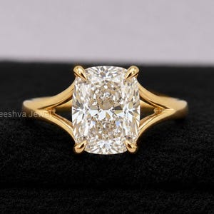 May include: A gold ring with a large, rectangular, clear gemstone. The ring has a split shank design, with the band splitting into two parts on either side of the gemstone. The gemstone is set in a four-prong setting.