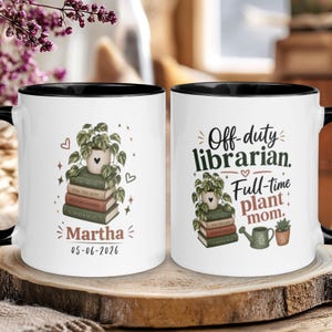 Può includere: Due tazze in ceramica bianca con bordi e manici neri. Una tazza presenta una pila di libri sormontata da una pianta in vaso, il nome Martha e la data 05-06-2026. L'altra tazza riporta il testo Off-duty librarian. Full-time plant mom.