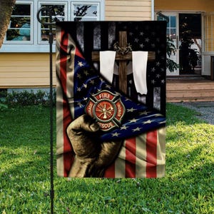 May include: A garden flag featuring an American flag design with a firefighter's emblem and a cross. The flag has a distressed look with red, white, and blue colors. The firefighter emblem reads "Courage, Honor, Rescue."
