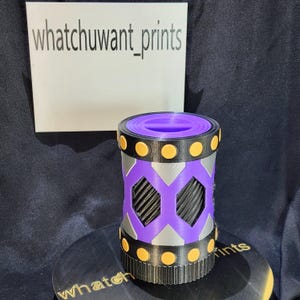 May include: A cylindrical 3D-printed object with a purple interior and a black and silver exterior. The design features geometric patterns and orange circular accents. The text "whatchuwant_prints" is visible.