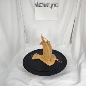 Può includere: Un modello architettonico color beige dell'hotel Burj Al Arab, posto su una base circolare nera. Il modello è dettagliato con elementi strutturali visibili. La base ha il testo "whatchuwant_prints" su sfondo bianco.