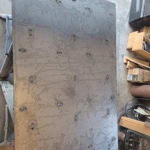 May include: Large, rectangular metal sheet with a textured, mottled surface. The sheet has numerous small, rectangular metal clips evenly spaced across its surface. The metal appears to be a dark grey colour.
