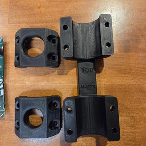 May include: Four black 3D-printed mounting brackets. Two brackets have a circular opening, and the other two have a curved design. The brackets are designed to be mounted together. The word "Top" and "Bottom" are printed on one of the brackets.