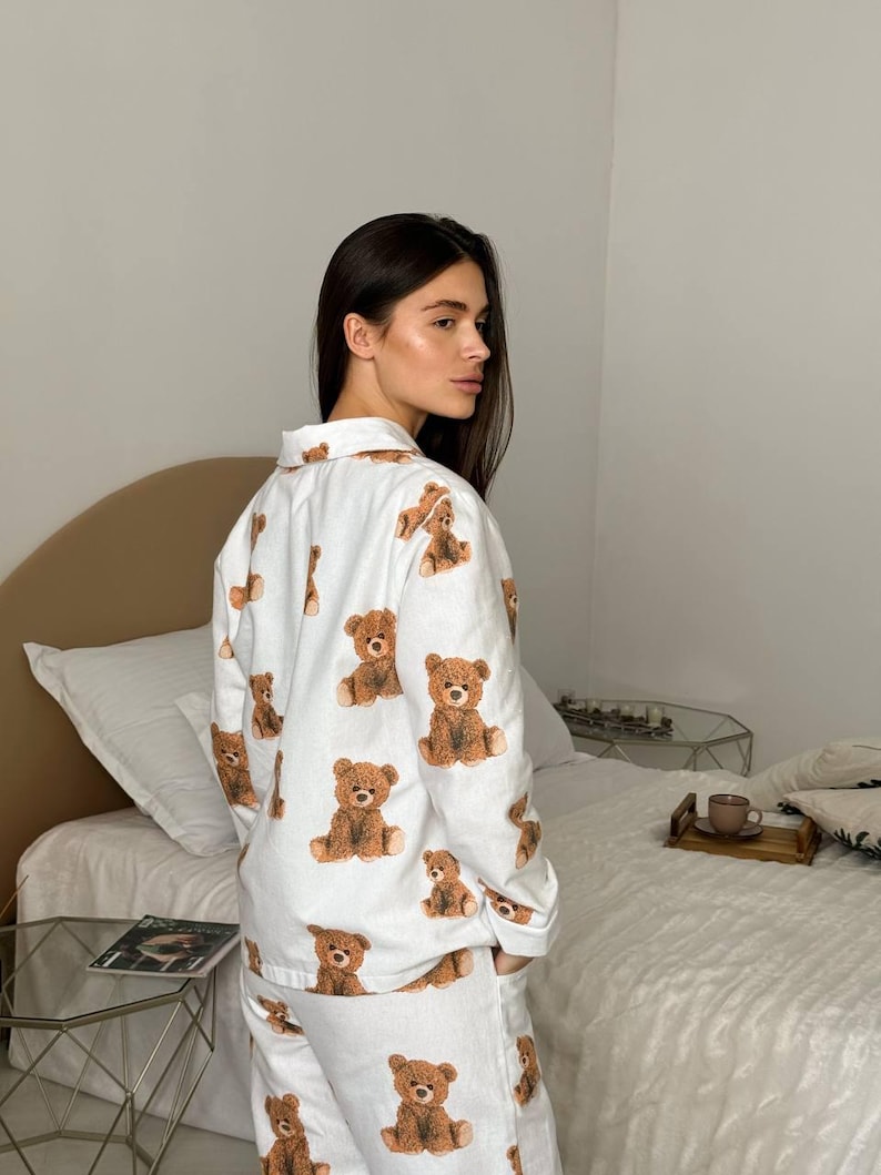以下が含まれることがあります： 茶色のテディベアの繰り返し模様が特徴の白いパジャマセット。長袖トップスとパンツは柔らかい生地で作られています。パジャマは快適さとリラックスのために設計されています。