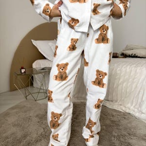 以下が含まれることがあります： 茶色のテディベアの繰り返し模様が特徴の白いパジャマセット。セットには、ボタンダウンシャツとパンツが含まれています。パジャマは柔らかい生地でできており、寝間着やラウンジウェアに適しています。
