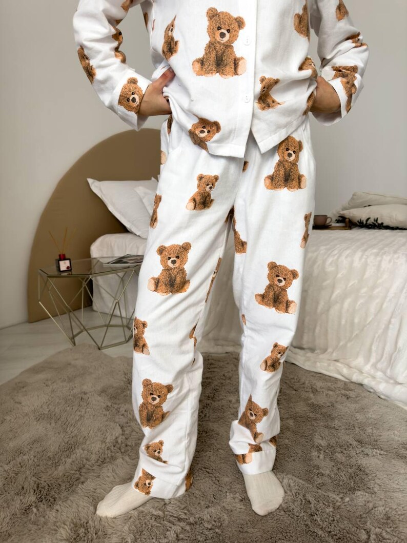 以下が含まれることがあります： 茶色のテディベアの繰り返し模様が特徴の白いパジャマセット。セットには、ボタンダウンシャツとパンツが含まれています。パジャマは柔らかい生地でできており、寝間着やラウンジウェアに適しています。
