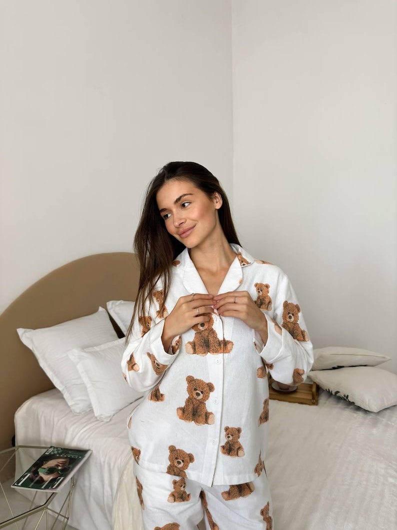 以下が含まれることがあります： 茶色のテディベアの繰り返し模様が特徴の白いパジャマセット。セットにはボタンダウンシャツとマッチするパンツが含まれています。パジャマは柔らかく軽い生地でできており、くつろいだり、眠ったりするのに最適です。