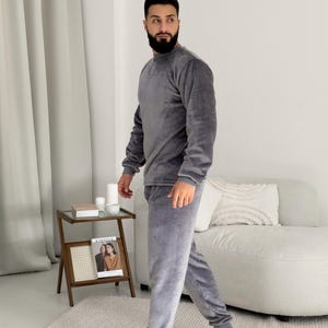 May include: A gray velour loungewear set, including a long-sleeved crew neck top and matching pants. The pants have a relaxed fit with elastic cuffs. The fabric appears soft and comfortable. The set is designed for casual wear.